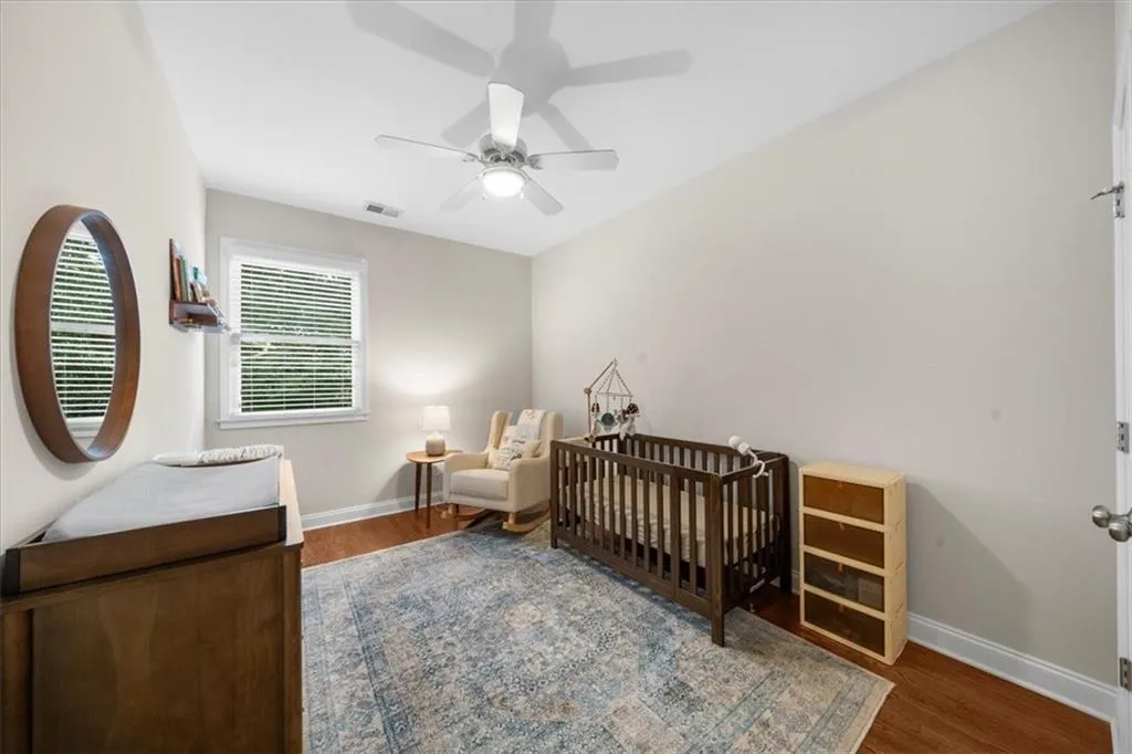 Bedroom with wood finished floors, ceiling fan, and a crib