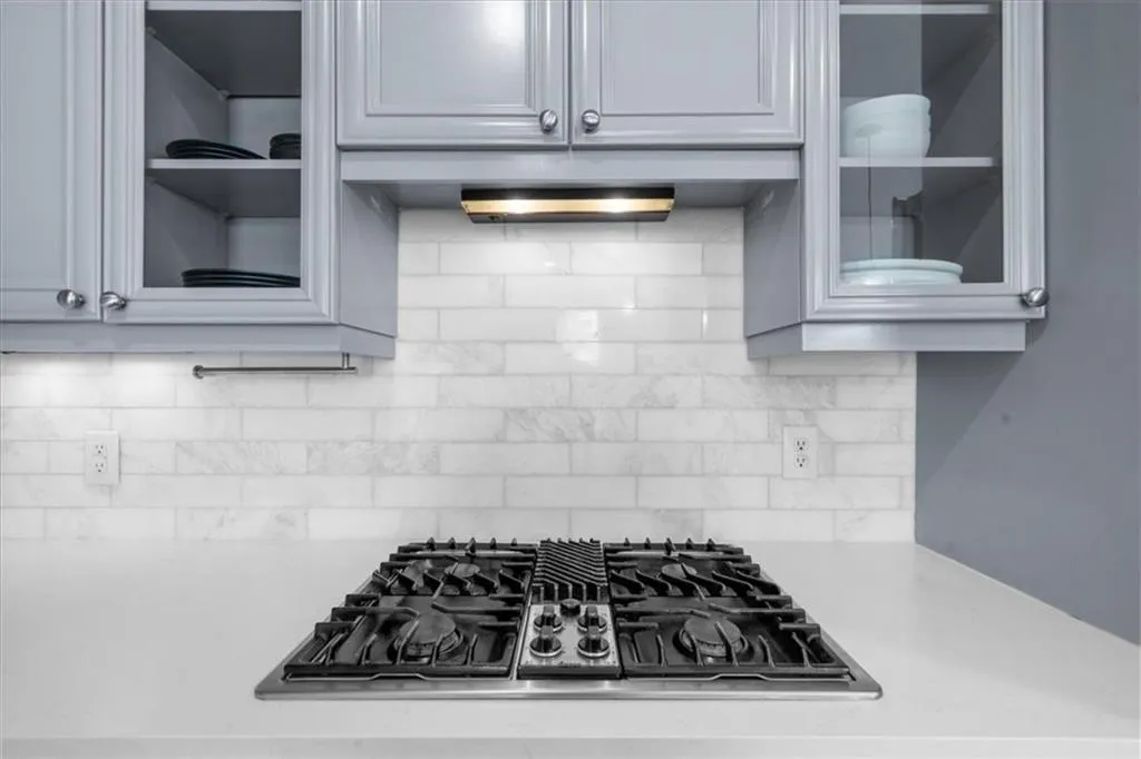 Kitchen with gas stovetop, glass insert cabinets, and backsplash
