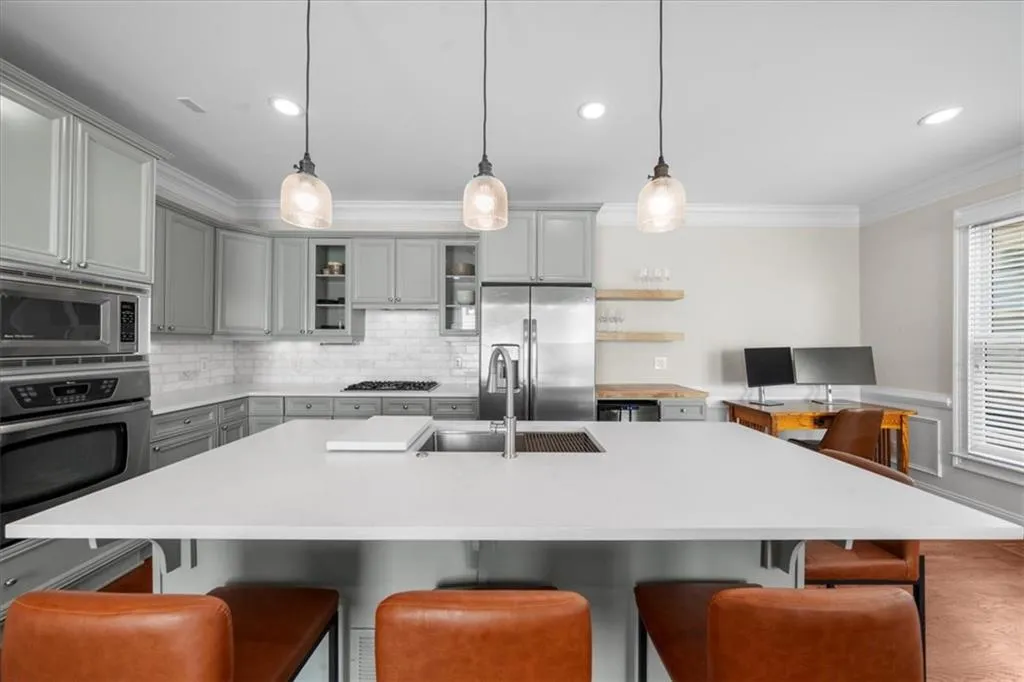 Kitchen featuring gray cabinets, appliances with stainless steel finishes, crown molding, backsplash, and light countertops