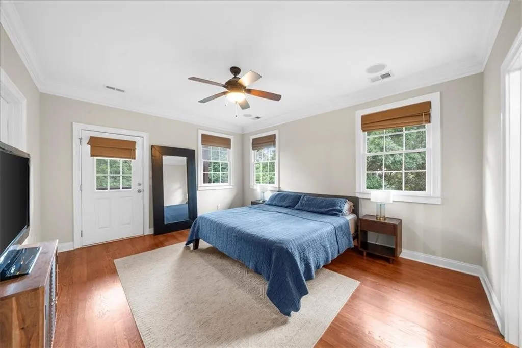 Bedroom with multiple windows, light wood-style floors, ornamental molding, and a ceiling fan