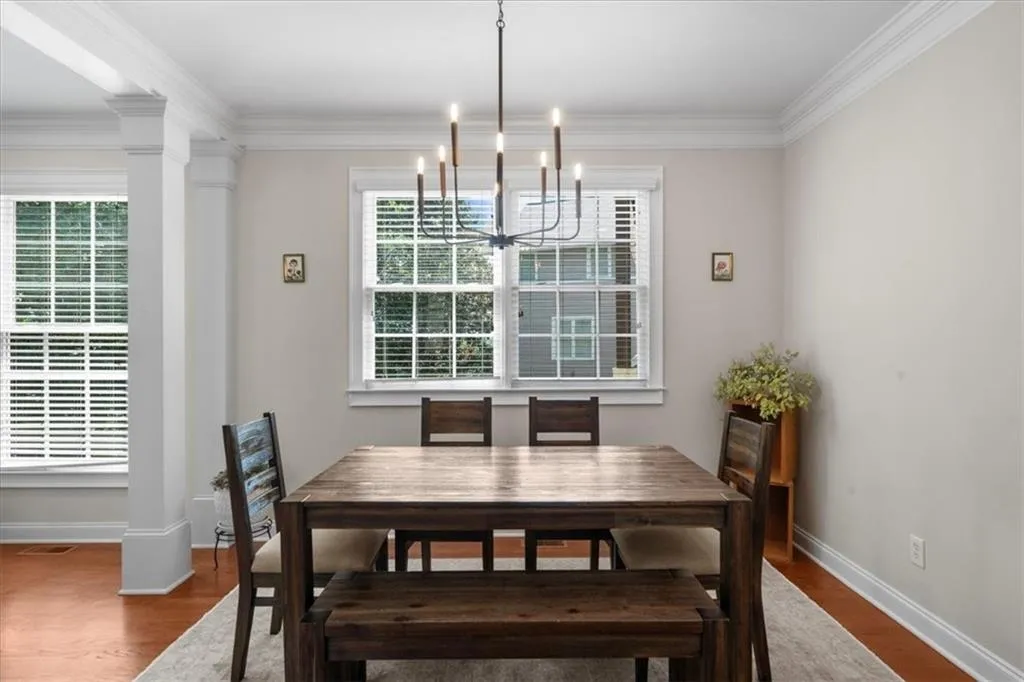 Dining area featuring a chandelier, wood finished floors, ornamental molding, and decorative columns