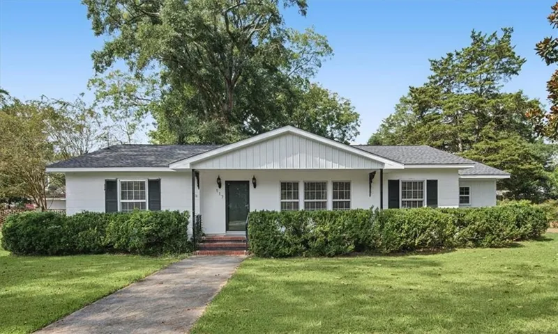 Single-story residence featuring a dark shingle roof, white brick exterior, dark shutters, and a covered porch entry