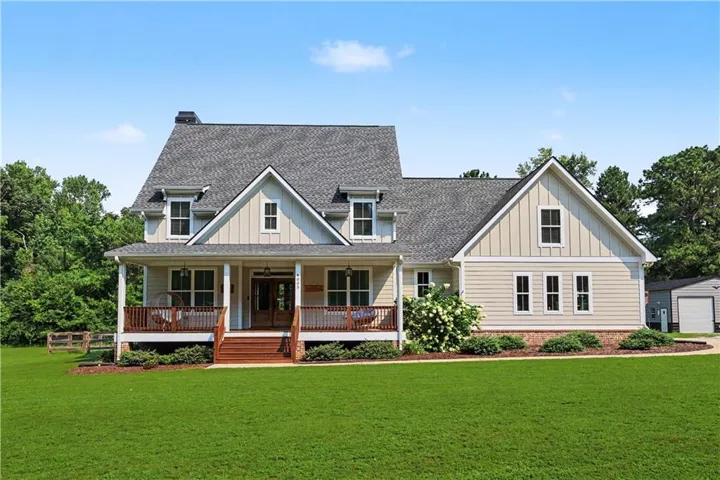 Craftsman-style home featuring a covered front porch with wood railings and steps, dormer windows, a shingle roof, and a detached garage