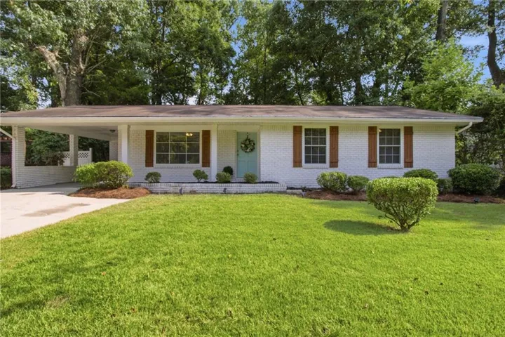 White brick exterior with a light blue entry door, wood shutters, and a covered carport