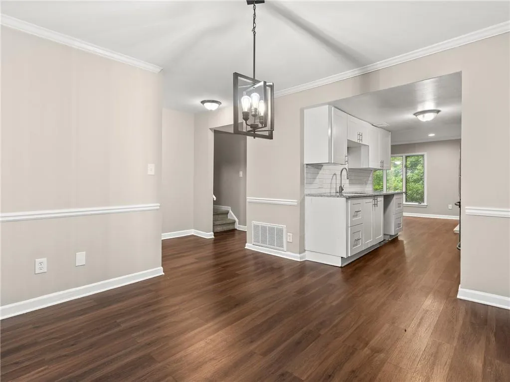 Unfurnished dining area featuring crown molding, dark wood-style floors, stairs, and a chandelier