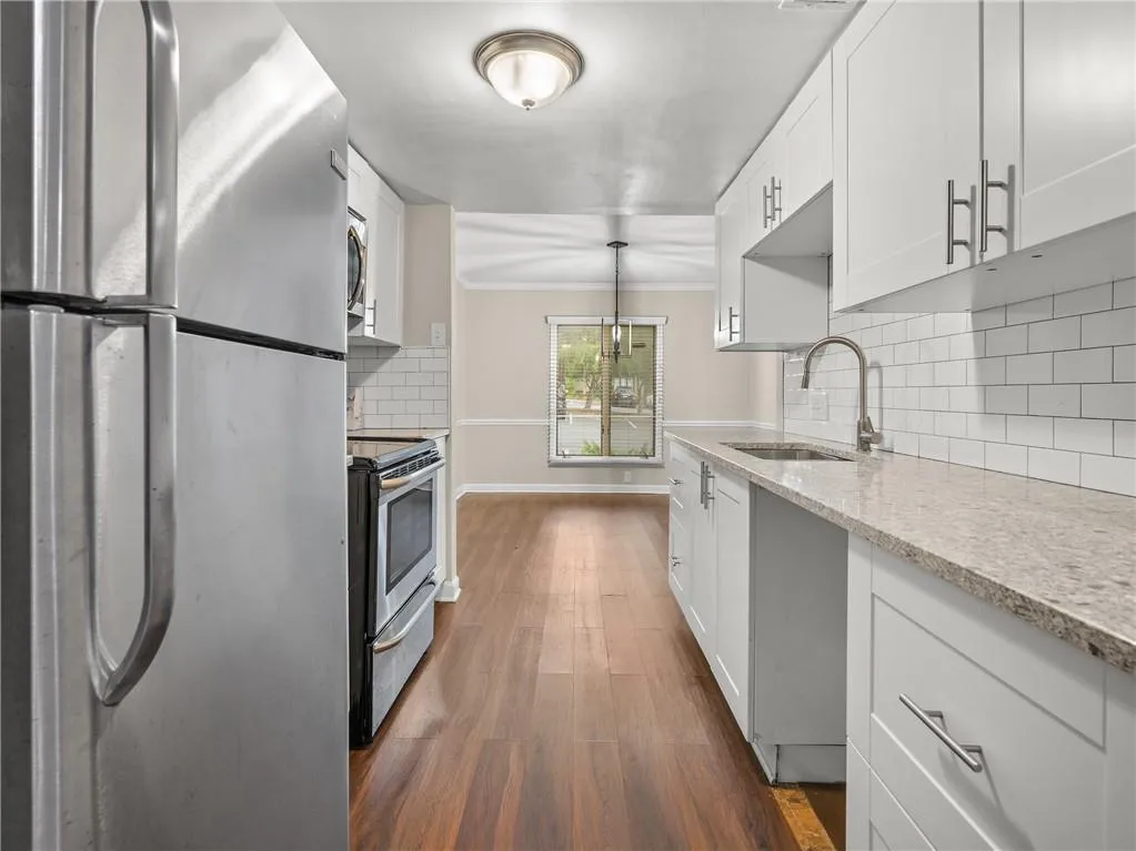 Kitchen featuring stainless steel appliances, backsplash, dark wood-style flooring, white cabinetry, and light stone countertops