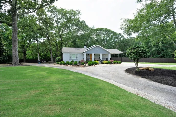 View of front facade with a chimney, curved driveway, a porch, and view of wooded area