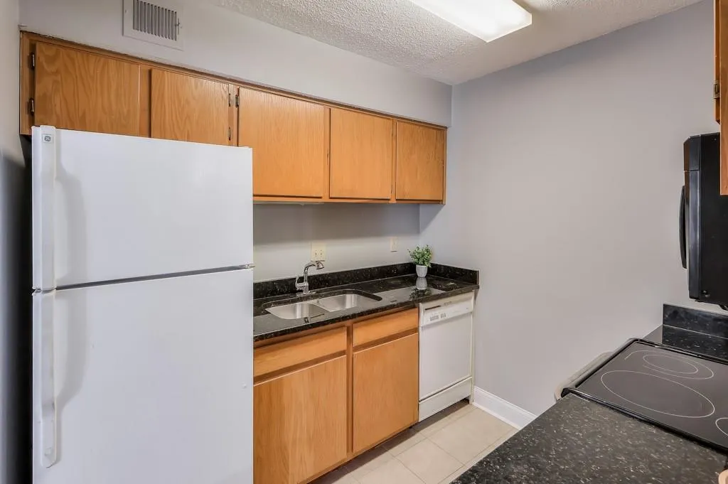 Kitchen with dark stone counters, light tile floors, sink, white appliances, and a textured ceiling