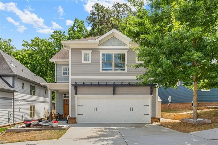 Two-story residence featuring light gray siding, white trim, a double garage with decorative hardware, an arched wood-finish entry door, and a pergola accent over the garage