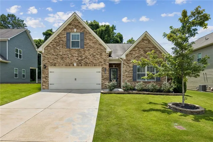 Brick facade home featuring a two-car garage, concrete driveway, front yard with mature landscaping, and a covered entry