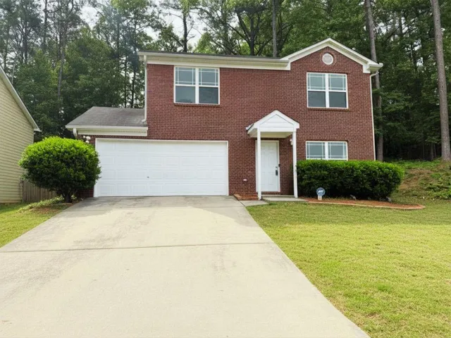 Brick exterior with white trim, featuring a two-car garage, a covered entry, and mature landscaping
