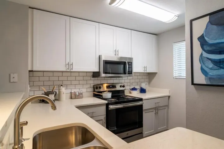 Kitchen with tasteful backsplash, appliances with stainless steel finishes, white cabinets, and sink