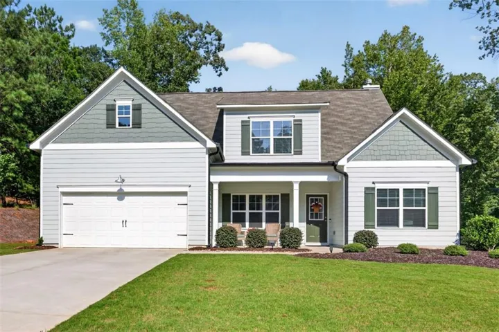 Colonial-style home featuring a two-car attached garage with paneled doors, crisp white siding, and multiple gabled rooflines
