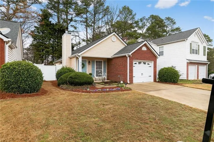 View of front of house with driveway, a chimney, brick siding, an attached garage, and covered porch
