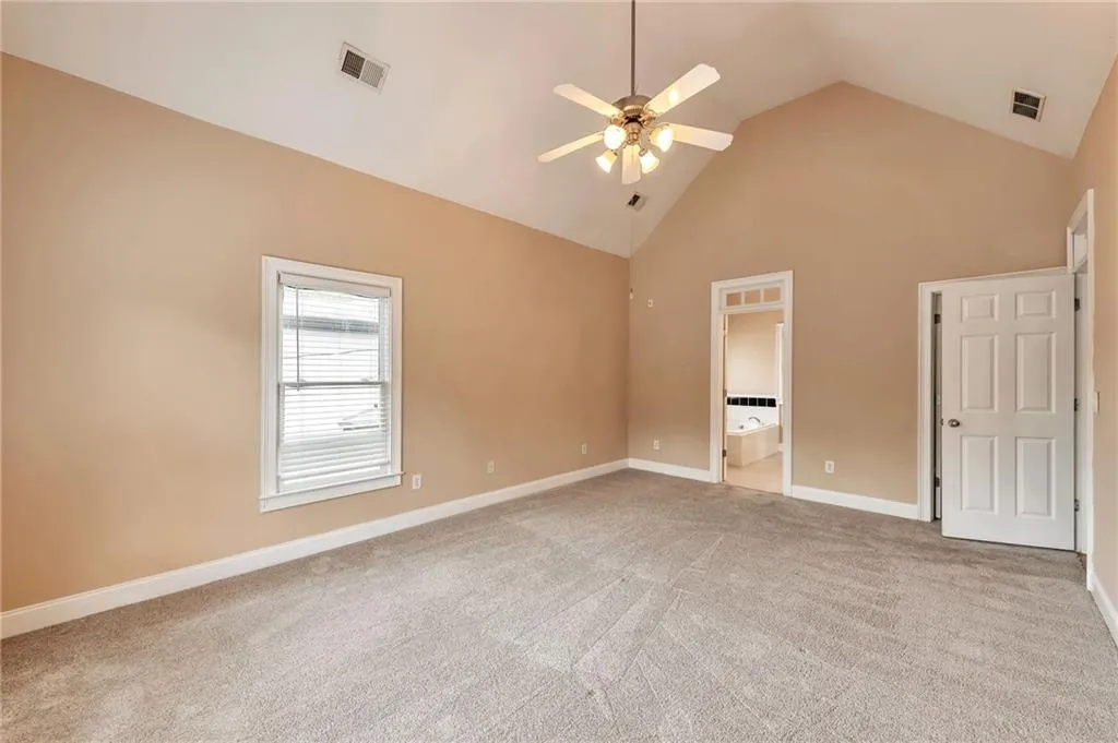 Unfurnished bedroom featuring high vaulted ceiling, light colored carpet, ceiling fan, and ensuite bathroom