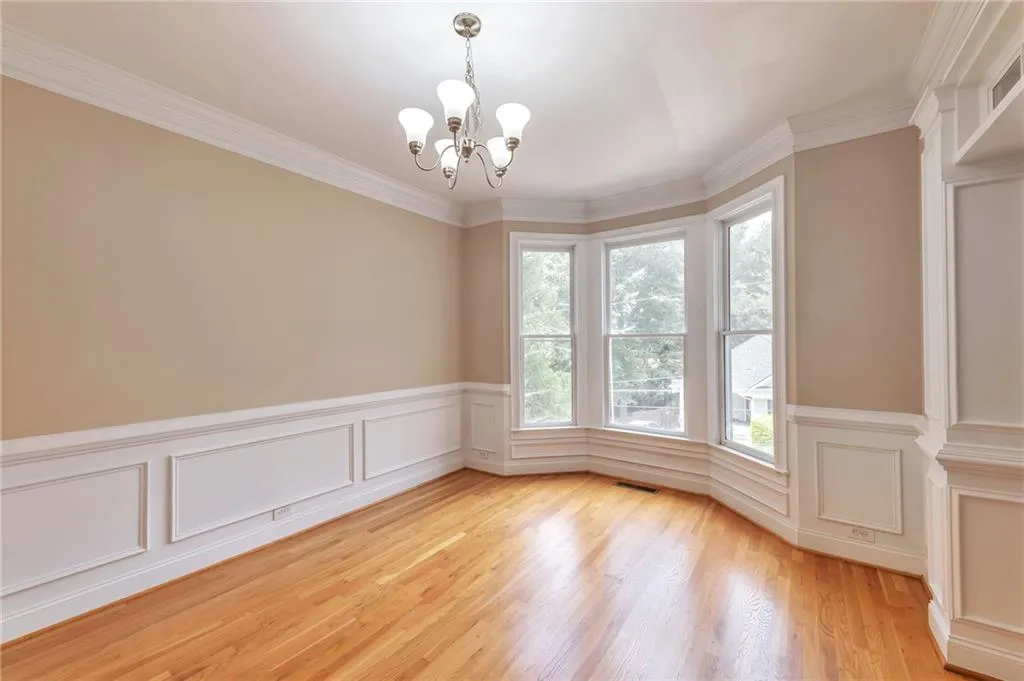 Unfurnished room featuring a chandelier, ornamental molding, light wood-type flooring, a wainscoted wall, and a decorative wall