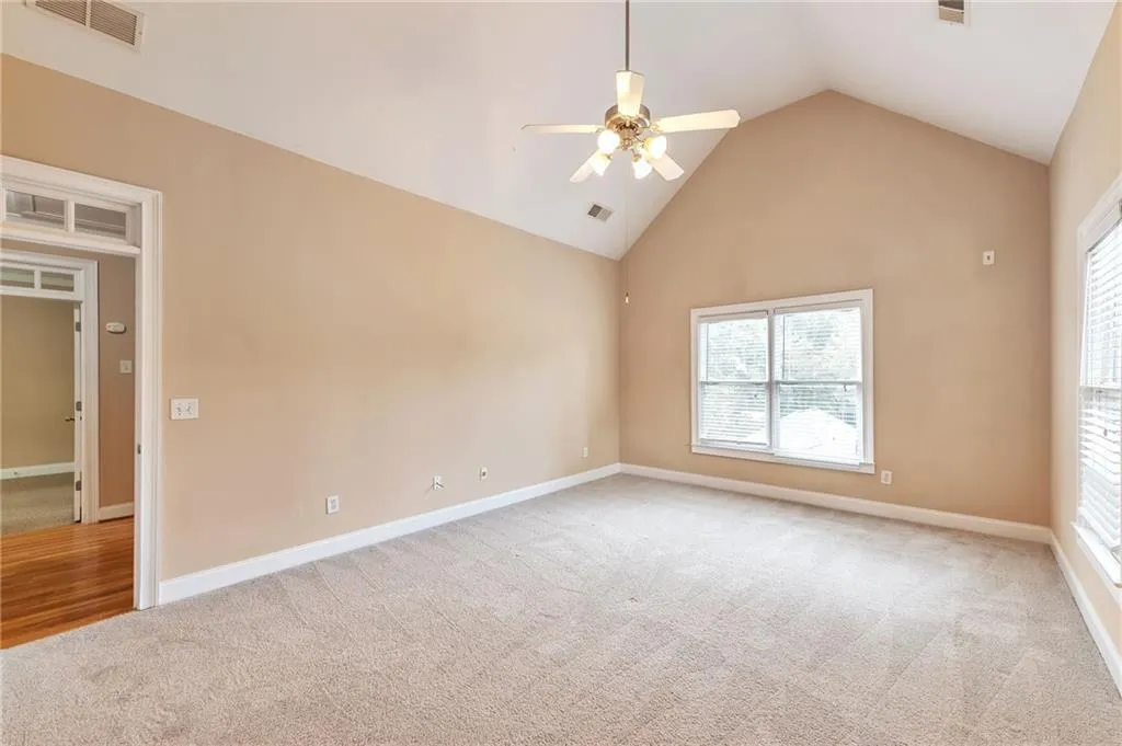 Unfurnished bedroom featuring light colored carpet, high vaulted ceiling, and ceiling fan