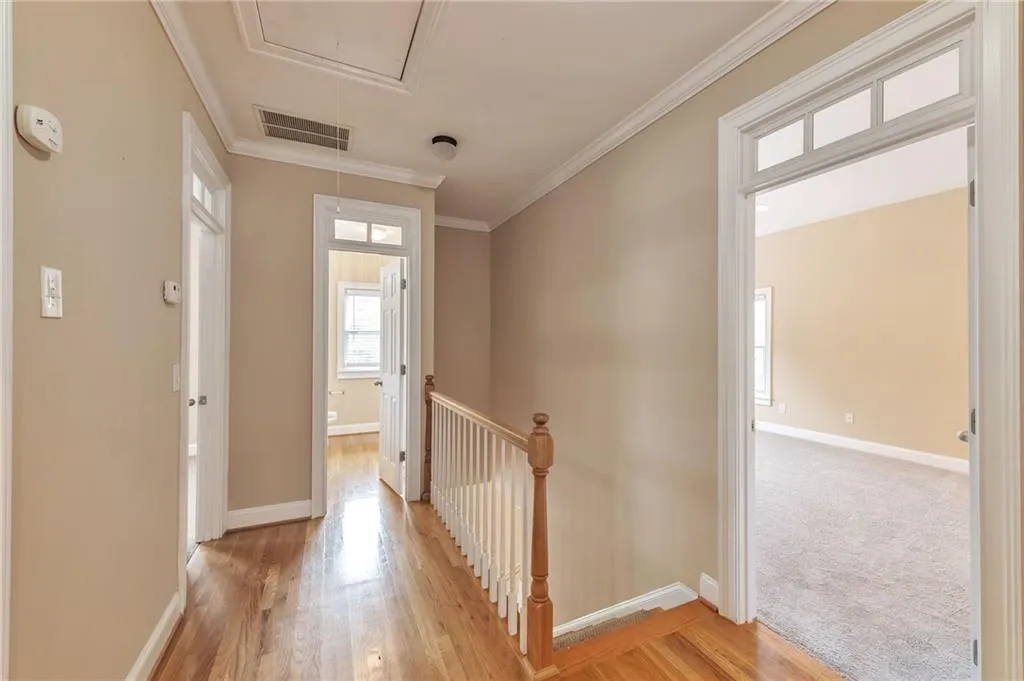 Hall with attic access, an upstairs landing, light wood-style floors, and crown molding