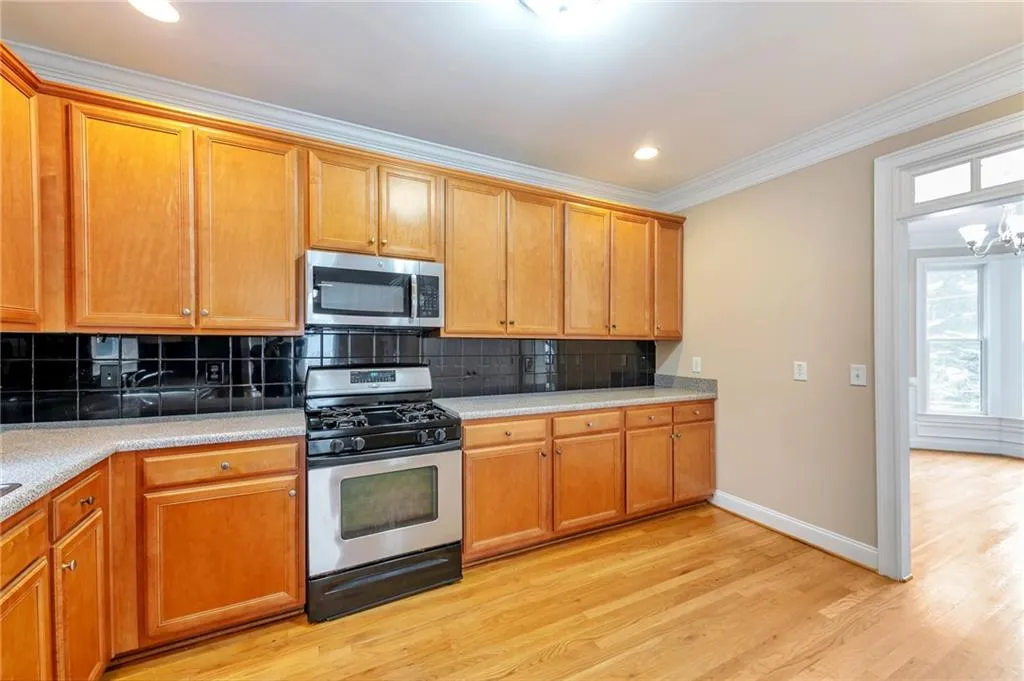 Kitchen featuring tasteful backsplash, appliances with stainless steel finishes, ornamental molding, brown cabinets, and light wood-type flooring