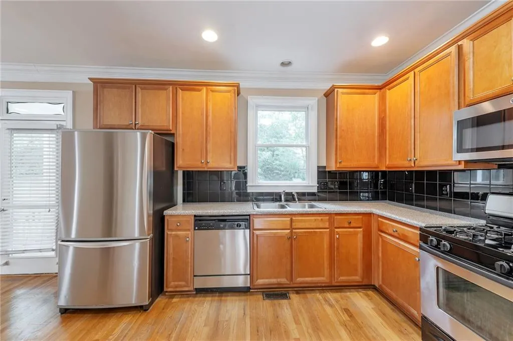 Kitchen with stainless steel appliances, ornamental molding, tasteful backsplash, brown cabinets, and light wood-style floors