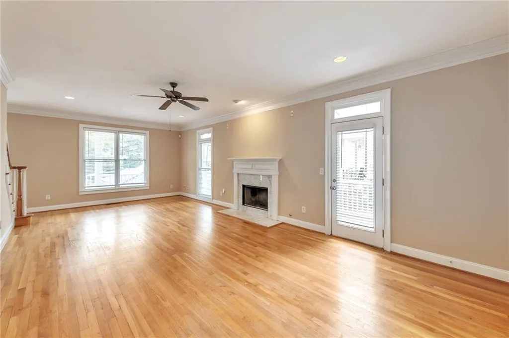 Unfurnished living room with crown molding, a premium fireplace, light wood-style flooring, a ceiling fan, and stairway