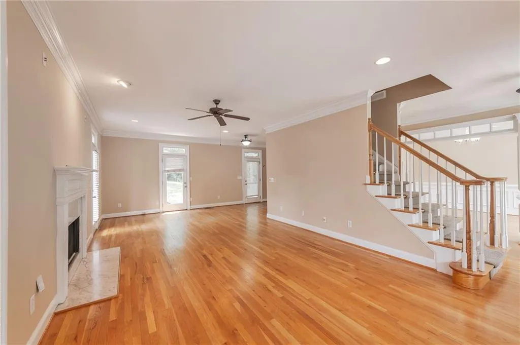Unfurnished living room with light wood-style floors, ornamental molding, a high end fireplace, a ceiling fan, and stairway