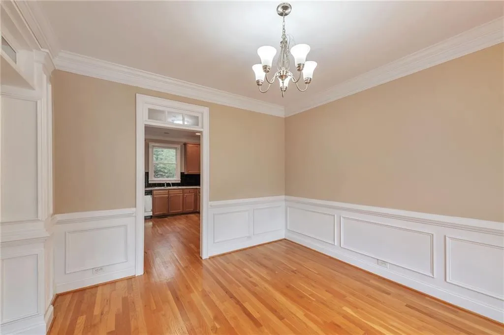 Unfurnished dining area with ornamental molding, light wood-style floors, a chandelier, a wainscoted wall, and a decorative wall