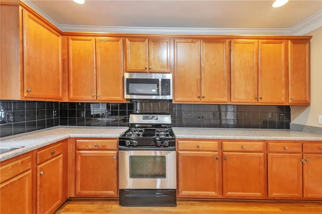 Kitchen featuring stainless steel appliances, brown cabinetry, decorative backsplash, ornamental molding, and light stone counters