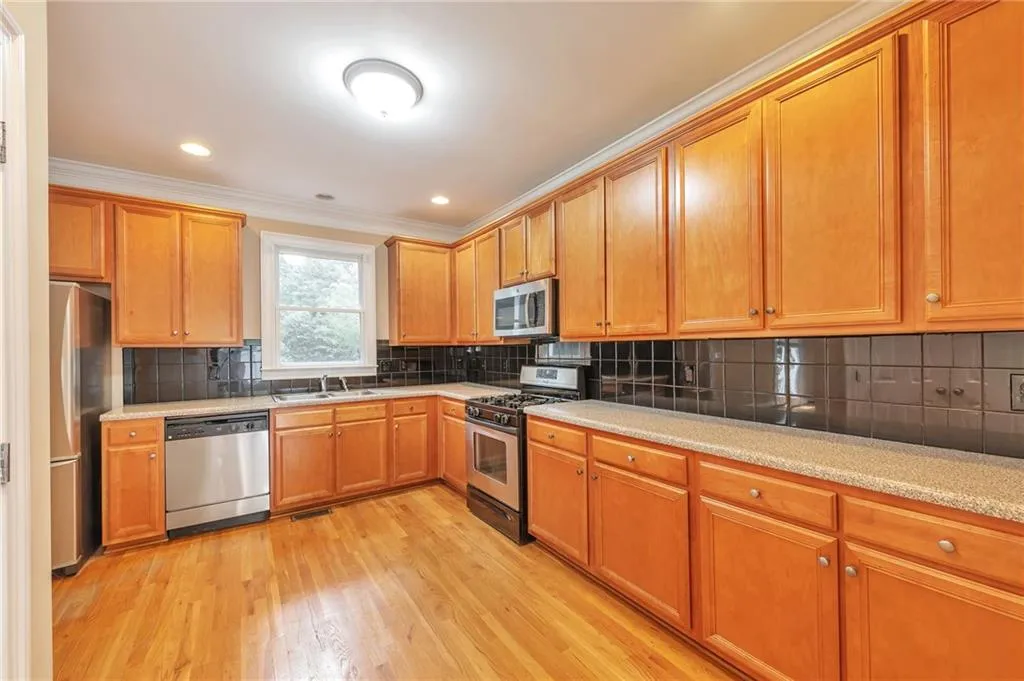 Kitchen with tasteful backsplash, appliances with stainless steel finishes, crown molding, brown cabinets, and light wood-style flooring