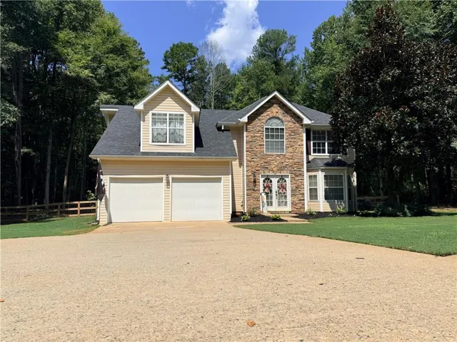 Two-story residence featuring a stone and siding exterior, dual dormers, an arched window, and a two-car garage