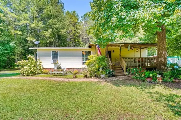 Single-story residence featuring light-colored siding, a covered front porch with wood railings and steps, and a lush green lawn