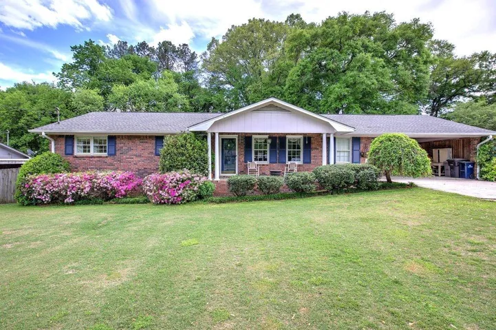 Brick facade home featuring a covered front entry, blue window shutters, and a carport