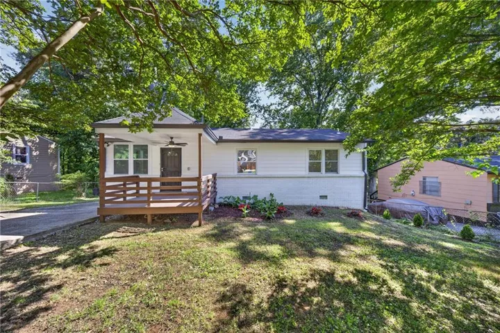 White exterior with a dark brown front door and a wood-finish porch featuring a ceiling fan