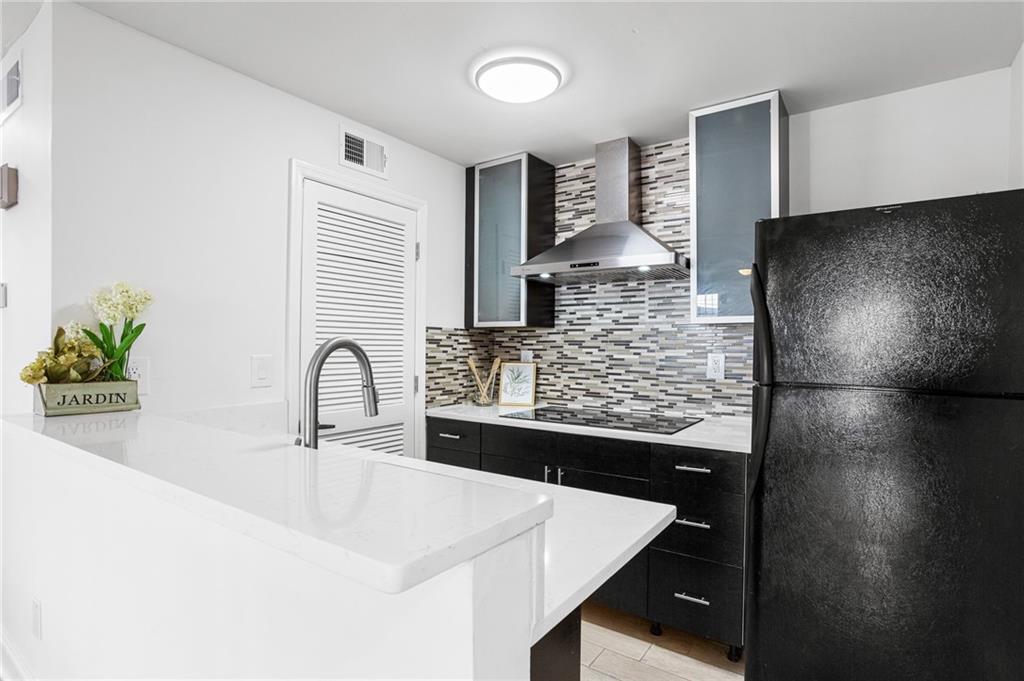 Kitchen with black appliances, tasteful backsplash, sink, and wall chimney range hood