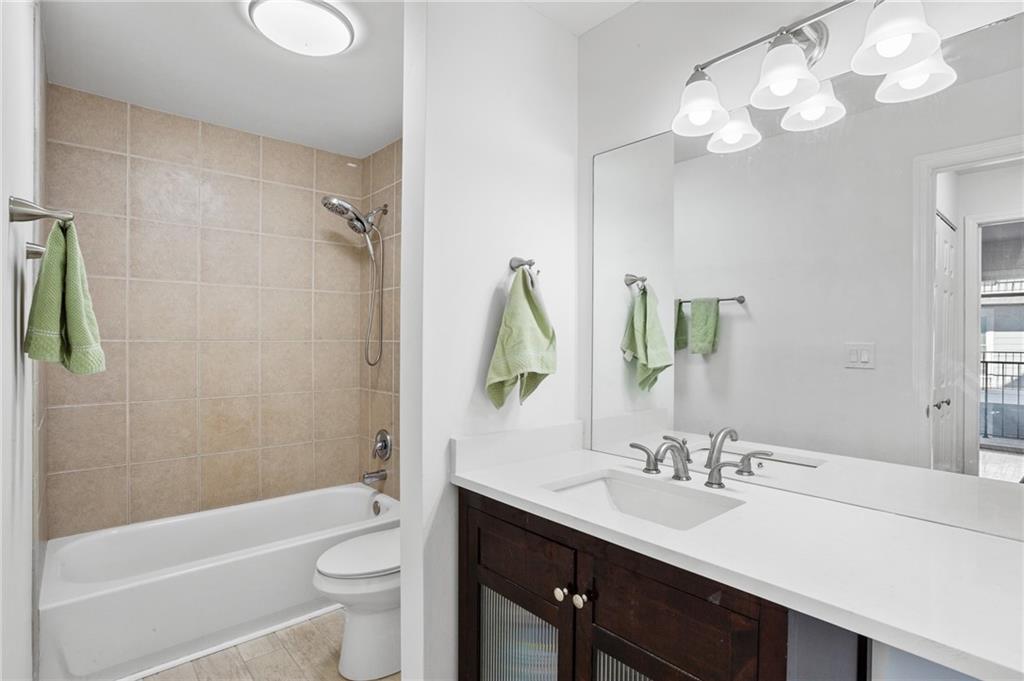Full bathroom featuring tiled shower / bath, large vanity, toilet, a notable chandelier, and hardwood / wood-style floors