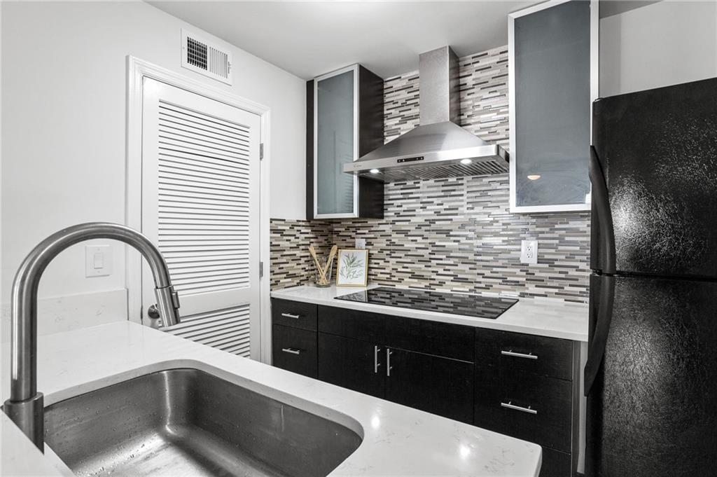 Kitchen with black appliances, wall chimney exhaust hood, light stone counters, backsplash, and sink