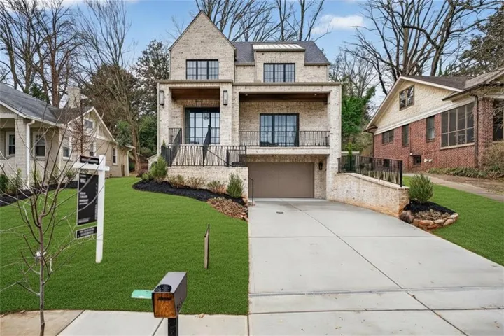 View of front of home featuring brick siding, a balcony, concrete driveway, a front lawn, and an attached garage