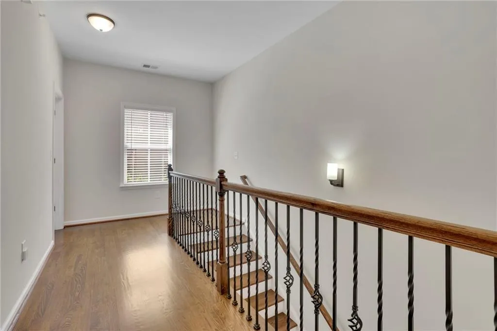 Hallway with baseboards, an upstairs landing, visible vents, and wood finished floors Hallway with baseboards, an upstairs landing, visible vents, and wood finished floors