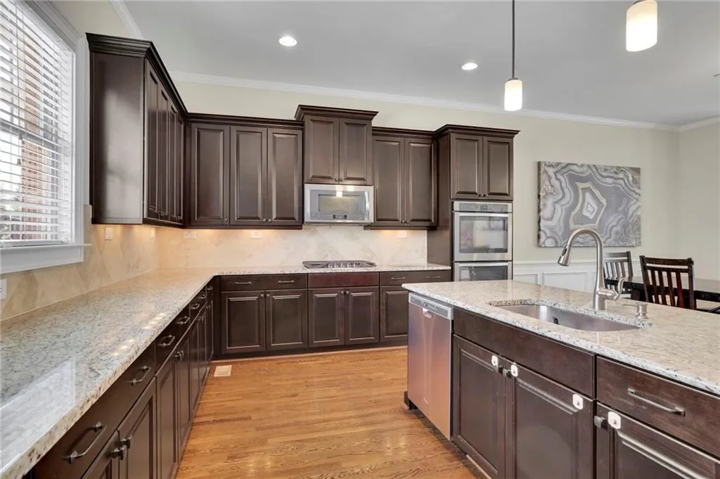 Kitchen with crown molding, a sink, hanging light fixtures, light wood-type flooring, and stainless steel appliances Kitchen with crown molding, a sink, hanging light fixtures, light wood-type flooring, and stainless steel appliances