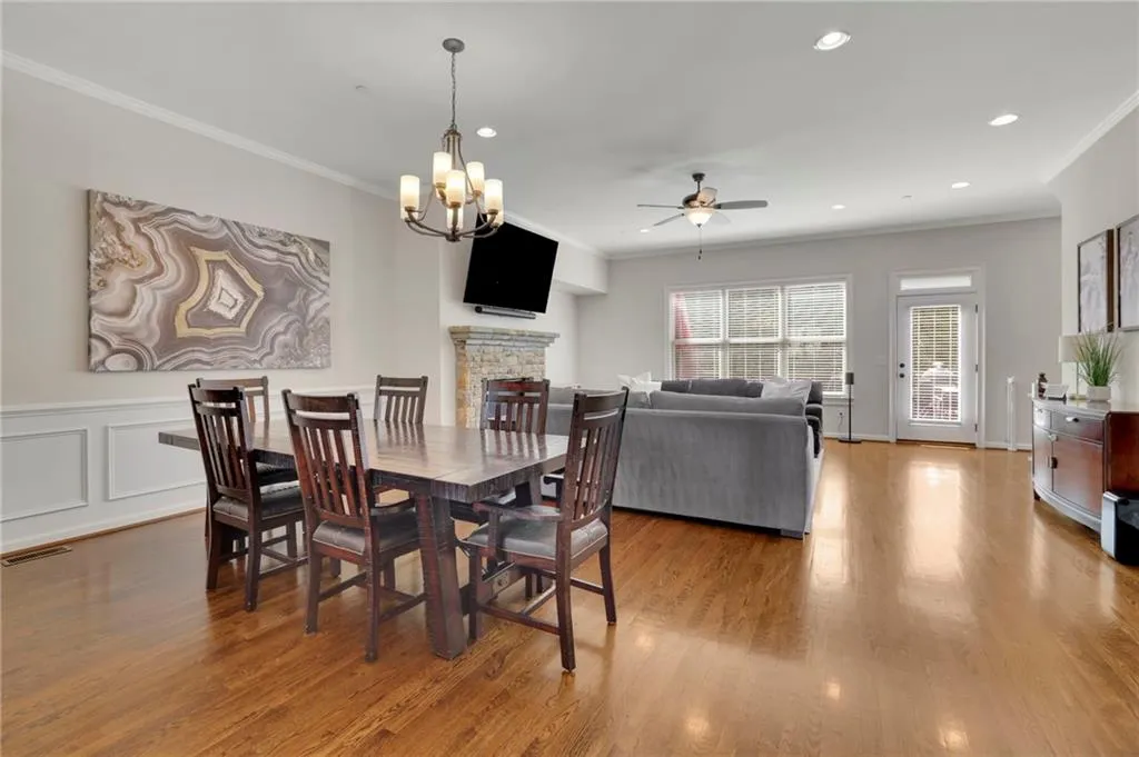 Dining space featuring ornamental molding, ceiling fan with notable chandelier, visible vents, a stone fireplace, and wood finished floors Dining space featuring ornamental molding, ceiling fan with notable chandelier, visible vents, a stone fireplace, and wood finished floors