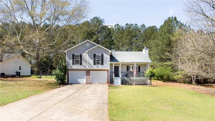 Split level home with a front lawn, a porch, an attached garage, concrete driveway, and a chimney