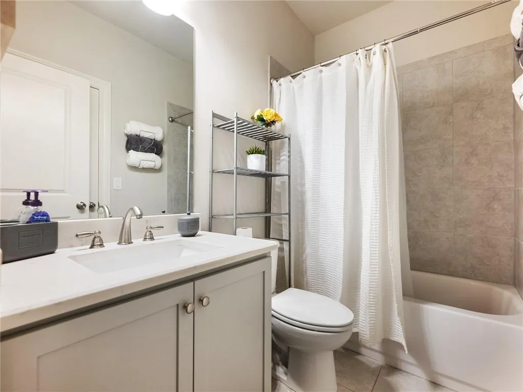 Bathroom featuring toilet, tile patterned floors, vanity, and shower / bathtub combination with curtain