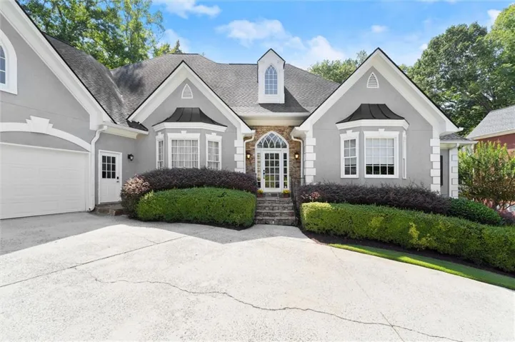 Hardcoat Stucco exterior with stone accents, arched entry door, bay window with metal roof detail, attached garage, and manicured landscaping