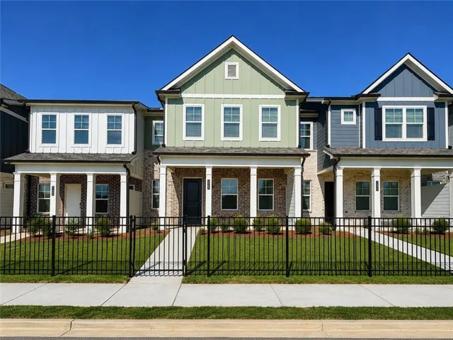 Contemporary townhome with a gabled roofline, brick and siding exterior, columned front porch, and black iron fencing