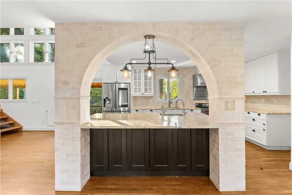 Bar featuring white cabinets, arched walkways, light stone countertops, hanging light fixtures, and light wood-style flooring