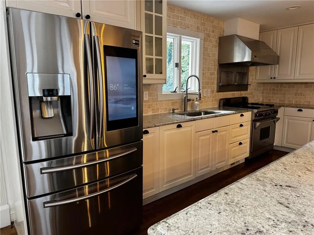 Kitchen with appliances with stainless steel finishes, extractor fan, dark stone countertops, and backsplash