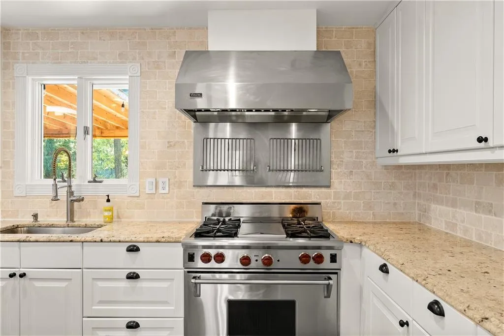 Kitchen featuring luxury range, range hood, light stone counters, and white cabinets