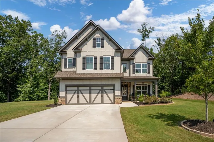 Contemporary Craftsman-style home featuring a two-car garage with decorative doors, a covered front porch with stone accents, and a concrete driveway