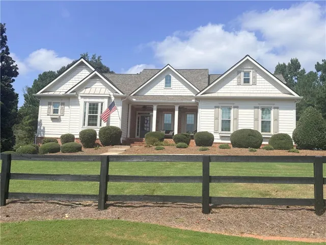 White siding exterior with a shingled roof, front porch with columns, and a black split-rail fence