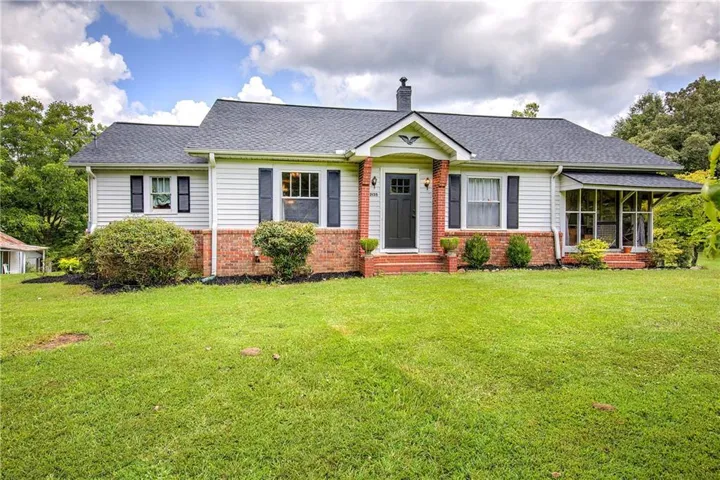 Exterior featuring a brick foundation, white siding, dark shutters, and a screened-in porch